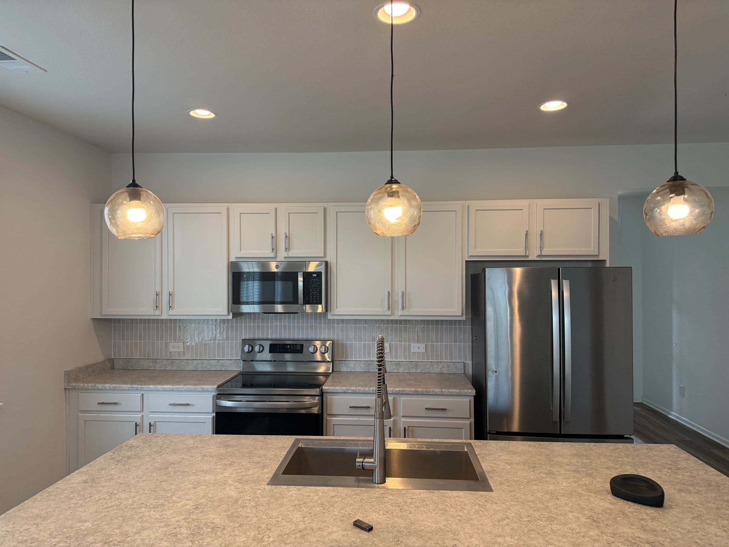 White shaker kitchen cabinets under three amber pendant lights